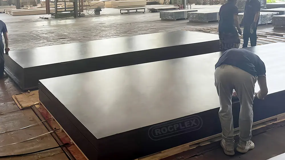 Film faced plywood manufacturing – black phenolic film panels stacked for formwork Stacks of black film faced plywood panels in factory with smooth phenolic film for concrete formwork